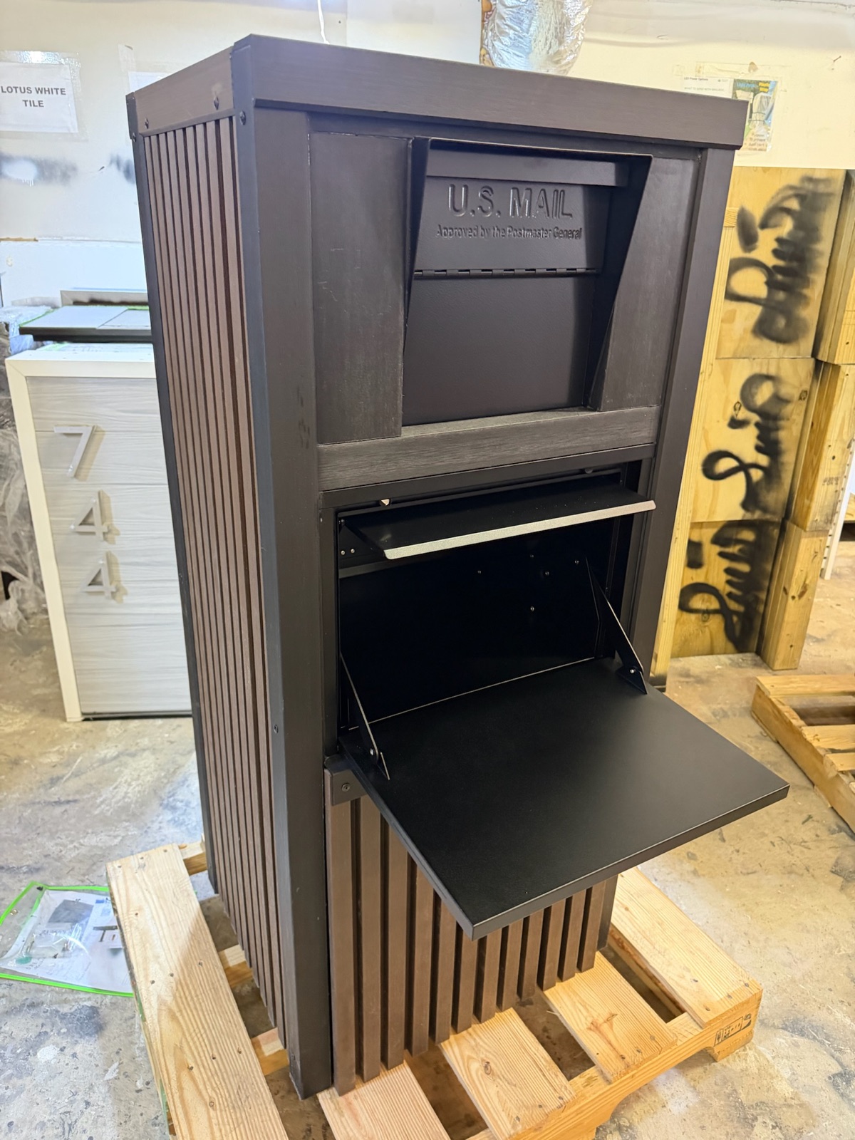 A black and gray curbside package vault with a top drop door and a locking retrieval door