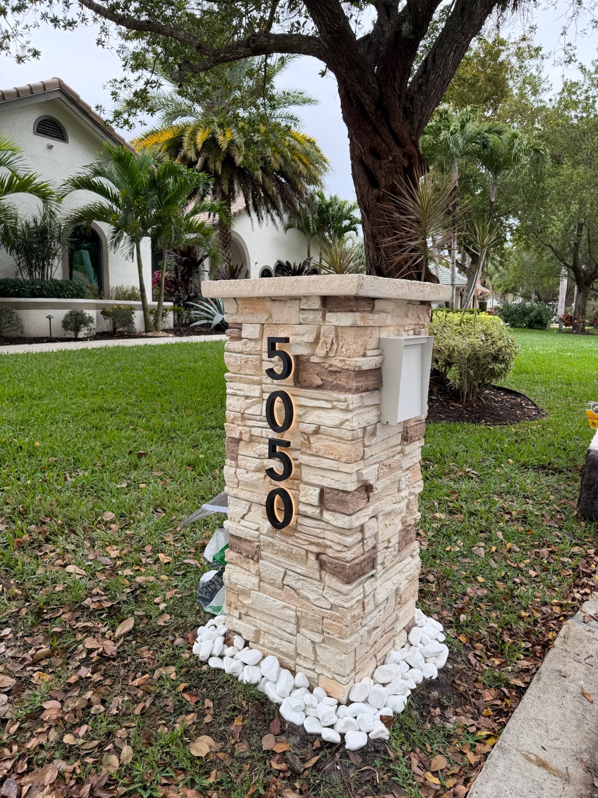 A slim modern pillar mailbox in a custom matte color at the curb of a flat-roof contemporary home