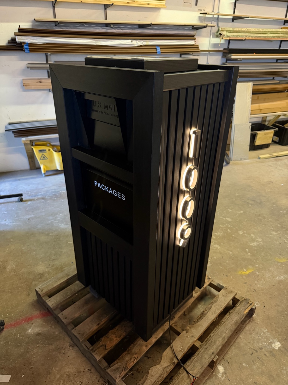 A black locking package vault standing at a curbside in wet, overcast Pacific Northwest weather