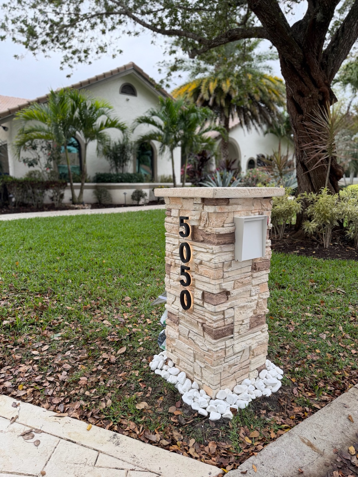 A faux stone pillar mailbox with a warm marbled finish standing at the curb of a Southwestern home