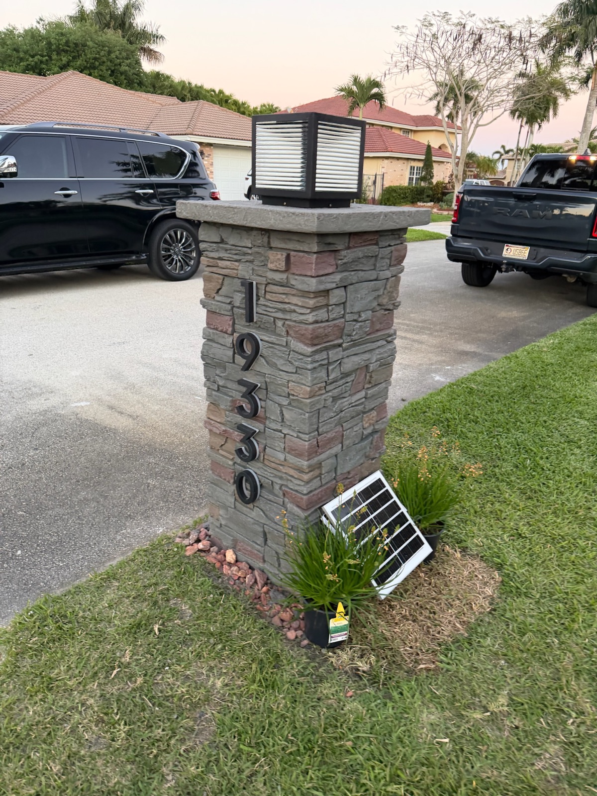 A black post-mounted locking mailbox set in a rock bed in front of a desert subdivision home