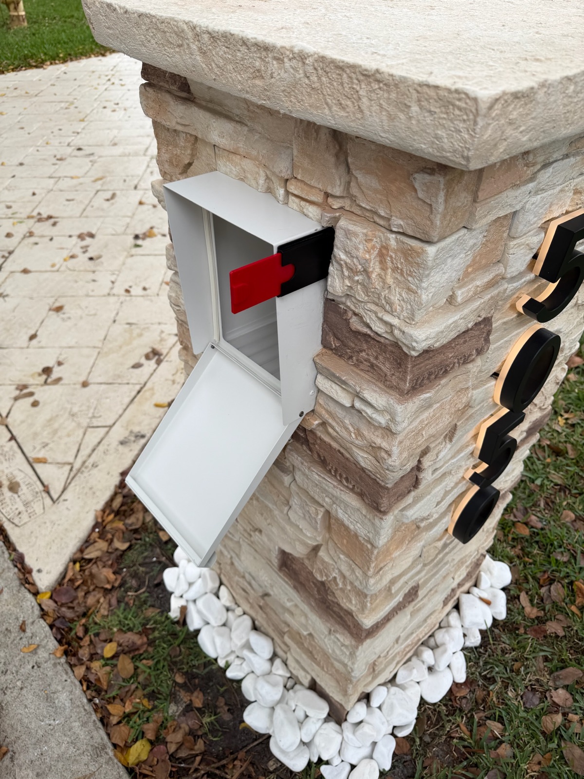 A stucco-look pillar mailbox shown in four color options against a warm exterior