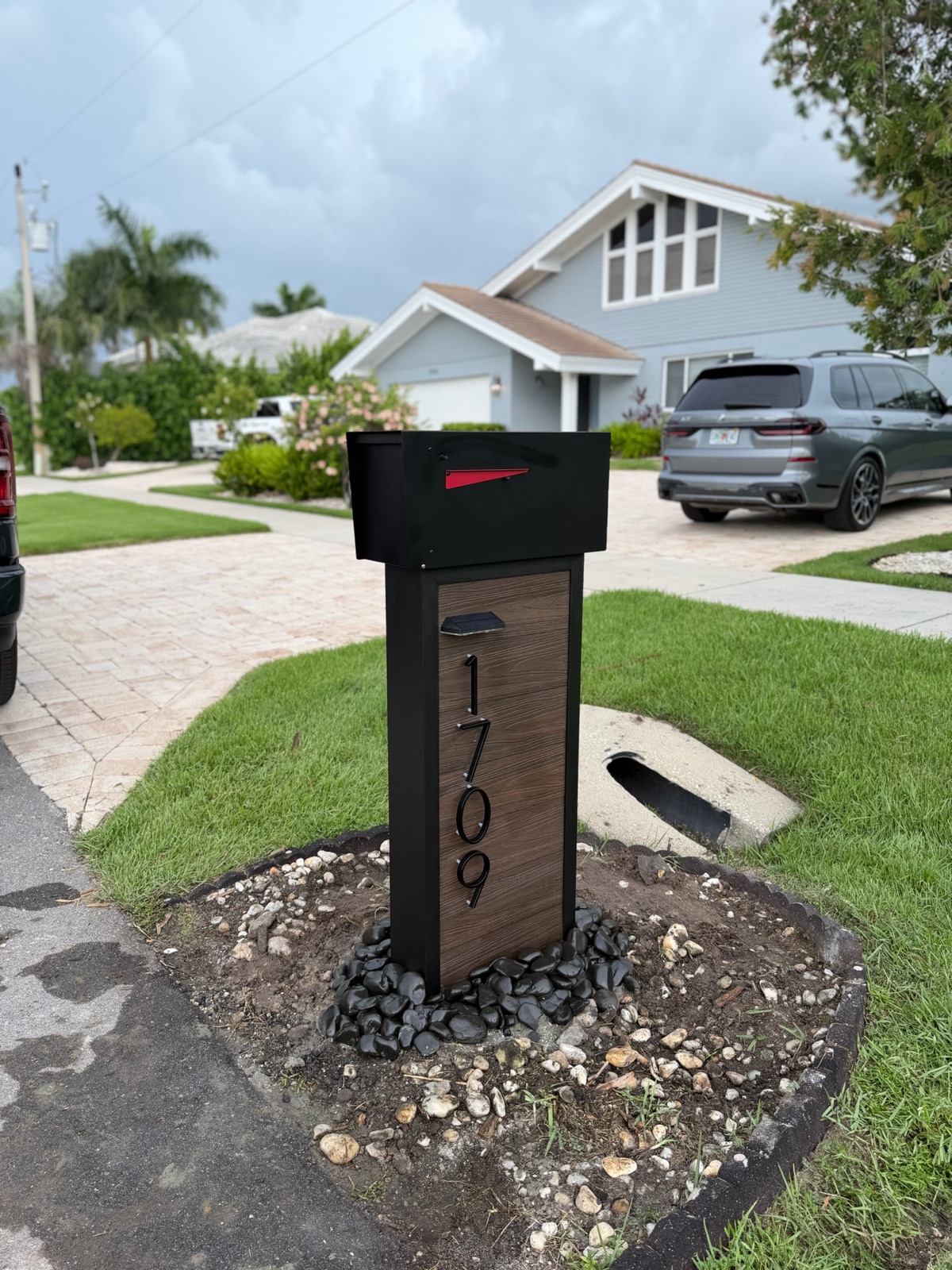 A newly set custom mailbox post with a rock bed at the curb of a Florida community, storm clouds building overhead