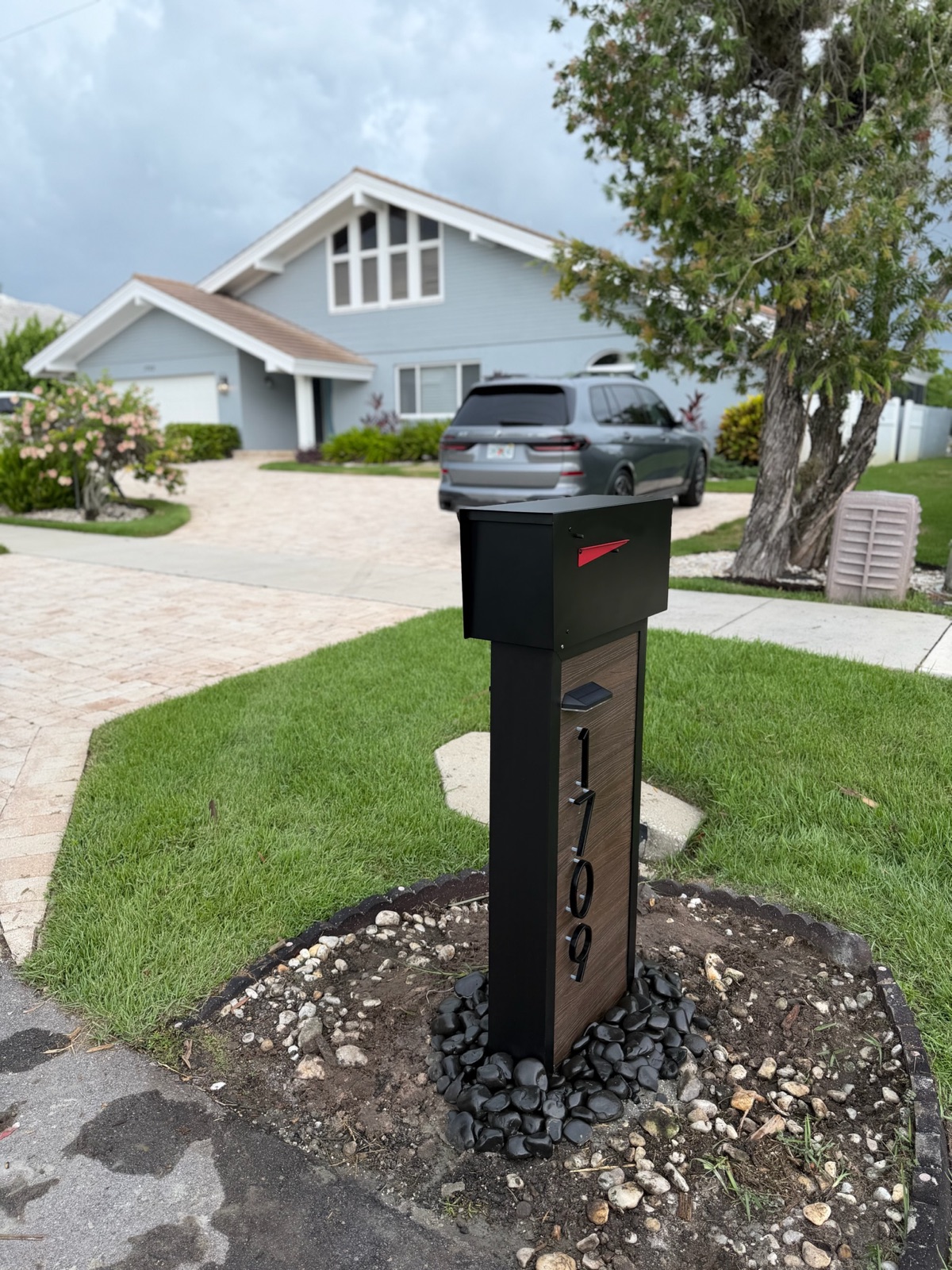 A finished custom mailbox and post at a community curb with the address numbers installed and the rock bed complete
