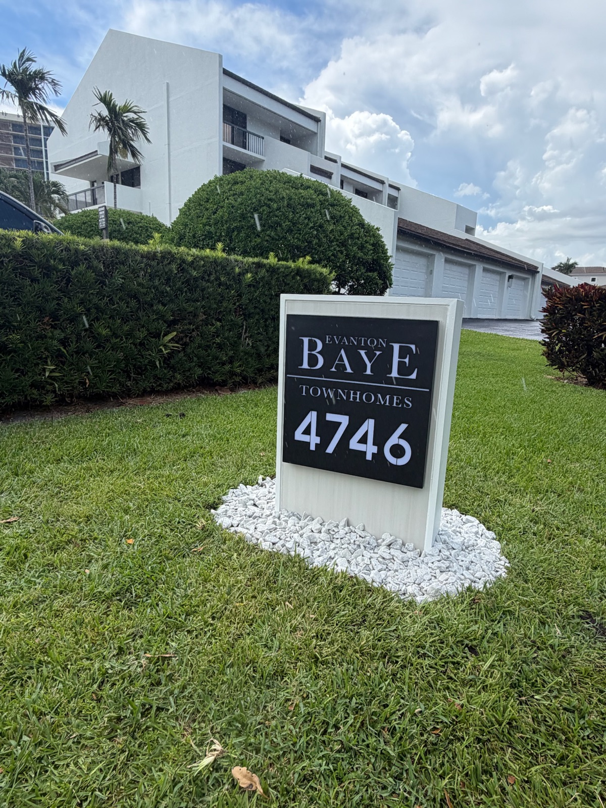 A powder-coated aluminum community mailbox and post set on a concrete footing with a rock bed at the base